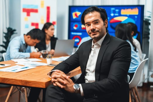 Portrait of businessman or analyst looking at camera with his colleague analyzing data analysis in dynamic business strategy investment planning meeting. Meticulous