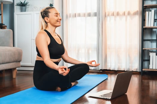 Senior woman in sportswear being doing yoga in meditation posture on exercising mat at home. Healthy senior pensioner lifestyle with peaceful mind and serenity. Clout