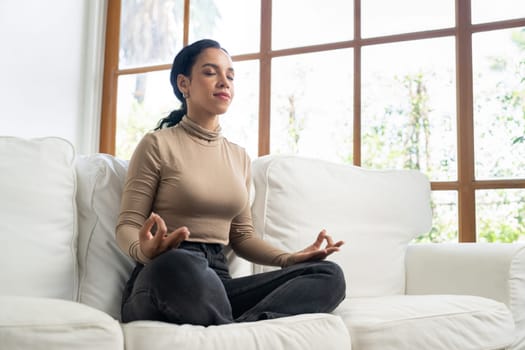 Young African American woman practice crucial mindful meditation at home living room for improving mental health strength and peaceful beautiful living