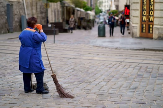 UKRAINE. Lviv. July 2023: A woman who cleans, sweeps the streets of the city, stands with her broom