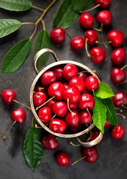 Cherry summer background. A large number of cherries with leaves on the table in a saucepan on a black background.