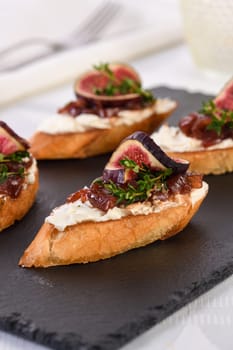 Canape or crostini with toasted baguette, cream cheese, onion jam, figs and fresh thyme on a slate board. Perfect as an aperitif for a holiday or party.