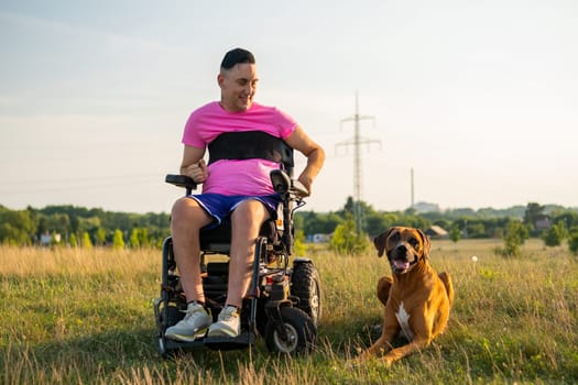 A happy disabled man with a wheelchair and his service dog at the park during sunset.