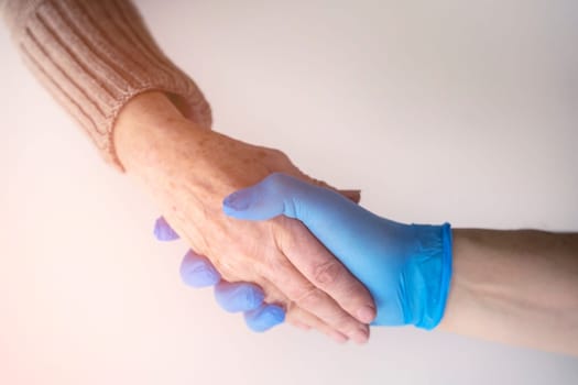 Handshake, caring, trust and support. A doctor's hand in a blue glove holds the hand of an elderly woman, a patient. Medicine and healthcare.