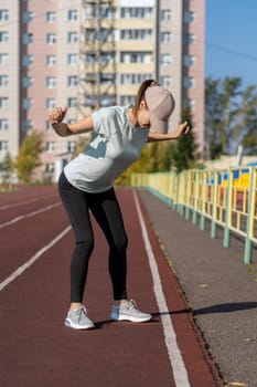 A young beautiful woman in sportswear plays sports at a local stadium. Exercise, jog and exercise at the beginning of the day. Healthy and active lifestyle.