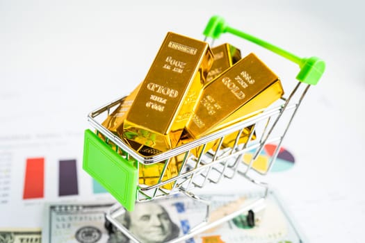 Gold bar in shopping cart on US dollar banknotes money and graph, economy finance exchange trade investment concept.