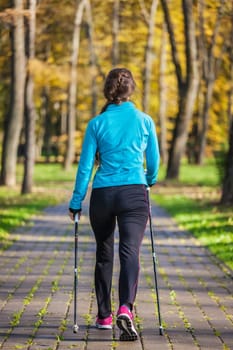 Nordic walking adventure and exercising concept - woman hiking withnordic walking poles in park