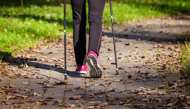 Nordic walking adventure and exercising concept - woman hiking withnordic walking poles in park