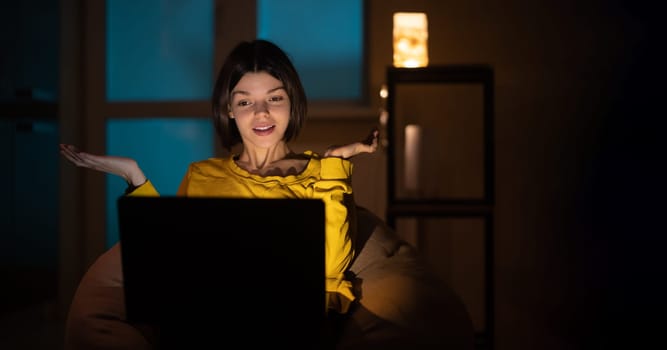 .The girl is surprised. She works on a laptop at home. In the evening creative woman works on a computer in her cozy living room.