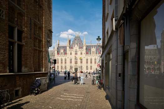 Bruges, Belgium – May 12, 2024: View through an alley to the market square, Grote Markt with the Provincial Palace in Bruges, Belgium
