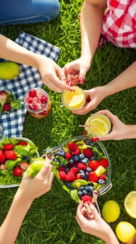 Women having picnic with lemonade, berries, salad and fruit on green grass in summer