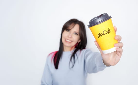 Cheerful woman with long dark hair holding McDonalds yellow coffee cup joyfully on white background - Ottawa ON Canada -2024-10-28