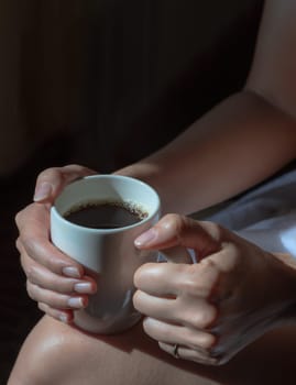 Close up of Comforting cozy female hands holding a coffee glass with the morning sunlight that shines through. Light and Shadow, use it as your Wallpaper, Poster and Space for text, Selective focus.