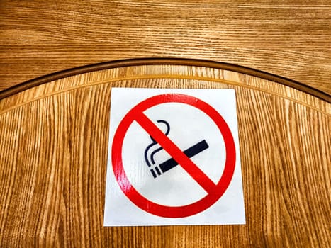 A no smoking sign is placed on a wooden table, indicating a smoke-free zone while indoors.