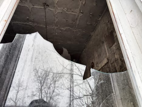 A broken window shows signs of neglect, exposing a dilapidated interior with peeling walls and debris nearby, indicating abandonment.