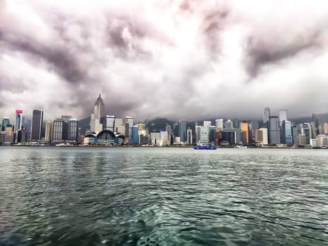 Hong Kong - April 06, 2024: Victoria Bay showcases the skyline of Hong Kong shrouded in fog, with towering buildings obscured by clouds. The water reflects the muted skyline on this overcast day.