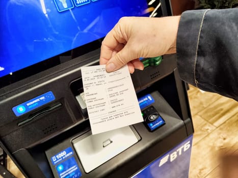 Kirov, Russia - September 29, 2024: Person retrieves transaction receipt from an automated teller machine in a busy city area on a bright day.