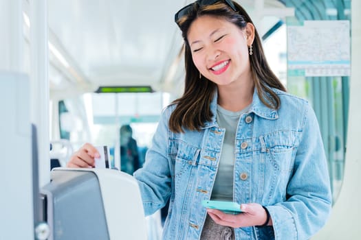 Cheerful young woman in a denim jacket validating her ticket inside public transport while holding a smartphone. She smiles as she uses the modern electronic system in an urban commuting setting.