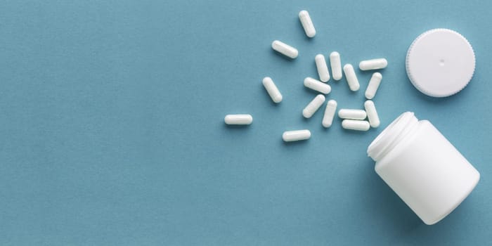 Pharmaceutical medicine capsules with the bottle on blue background and copy space for text. Medicine and health concepts include a jar with pills, antibiotic or vitamins