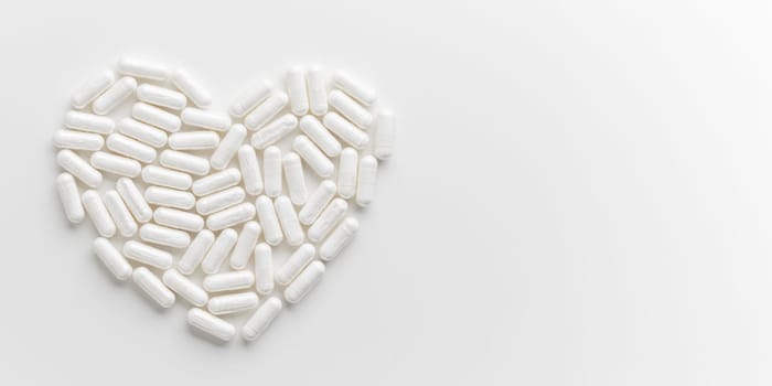 White Pills are arranged in heart shape on white table. Mock up background from top view with a copy space. Medical, pharmacy and healthcare. High-quality photo mock-up banner