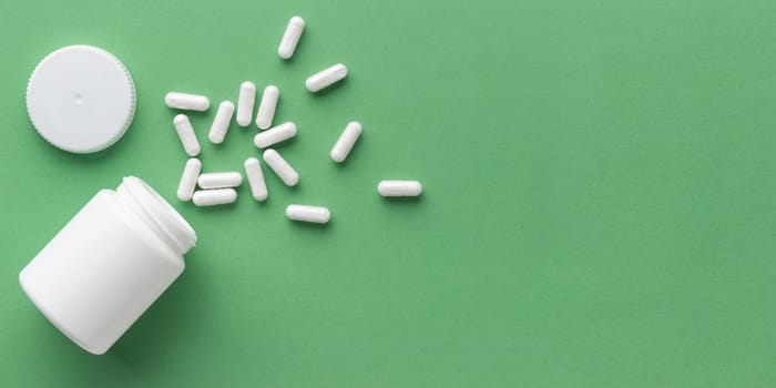 Pharmaceutical medicine capsules with the bottle on green background and copy space for text. Medicine and health concepts include a jar with pills, antibiotic or vitamins. High-quality mock-up banner