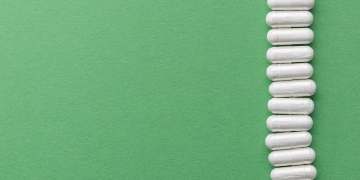 Scattered white medicine, pills or capsules on green table. Mock up background from top view with a copy space. Medical, pharmacy and healthcare. High-quality photo mock-up banner