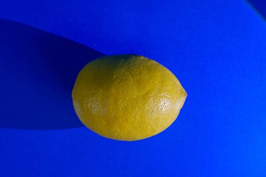 A single yellow lemon placed on a purple background with a prominent shadow. Close-up image showcasing vibrant contrast and minimal composition, ideal for food or design concepts