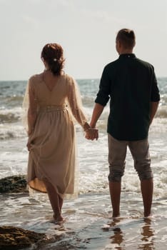 young couple in love on the seashore. they are standing in the sea water. a guy and a girl are holding each other's hands. and looking at the horizon. a girl in a dress a guy in a suit