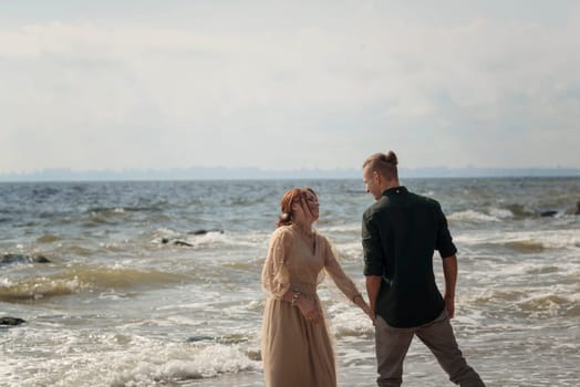 lovers and romantic newlyweds having fun on the seashore. couple dancing on the seashore. they holding hands and looking at each other. girl wearing beige dress, wind blowing their hair