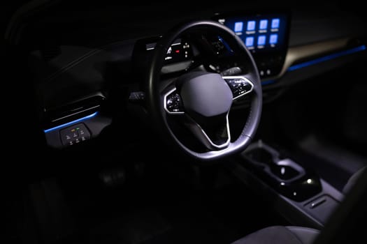 Black leather cockpit with blue ambient light. Electric car Interior view in the cabin. Expensive electric car interior with steering wheel. Interior of prestige modern electric car.