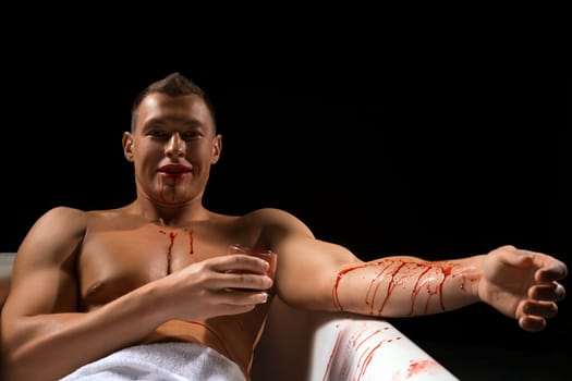 Handsome athletic man sitting in bath with glass of blood shot against black background