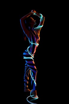 Slim girl wrapped in leds full-length shot in the dark room