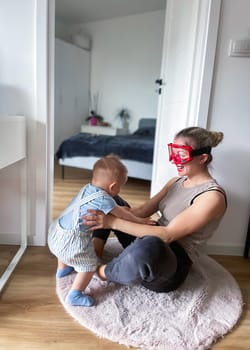 Young woman wearing big glasses having fun playing with her son. High quality photo