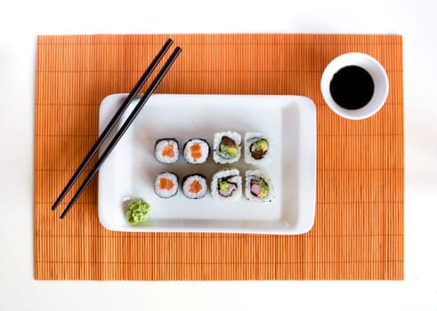 Delicious sushi rolls on white plate with chopsticks