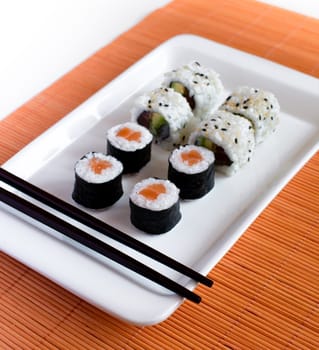 Delicious sushi rolls on white plate with chopsticks