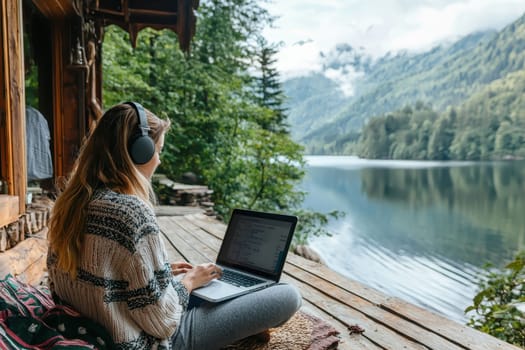 A young woman enjoys a tranquil working moment on a lakeside deck, surrounded by mountains and greenery, embodying the essence of remote work and relaxation.