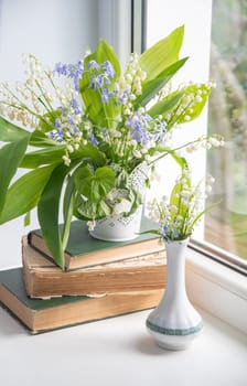 two bouquets of spring flowers on the windowsill, one of which stands on a stack of old books, lilies of the valley, creeping blue phlox,