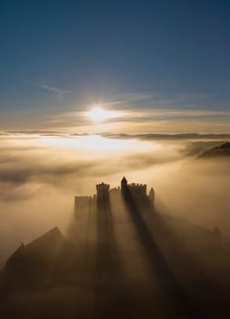 Chateau de Beynac stands majestically as the sun rises, casting long shadows through the mist, showcasing the enchanting beauty of Dordogne's landscape.