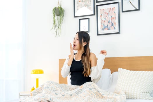 Young Asian woman action of yawn  during sit on bed in bedroom after wake up in the morning.
