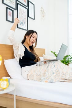 Vertical image of beautiful young Asian woman lean on bed with stretch lazily and relax in bedroom.