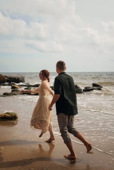 A smiling couple enjoys a carefree run on a sandy shore, waves gently breaking in the background. High quality photo