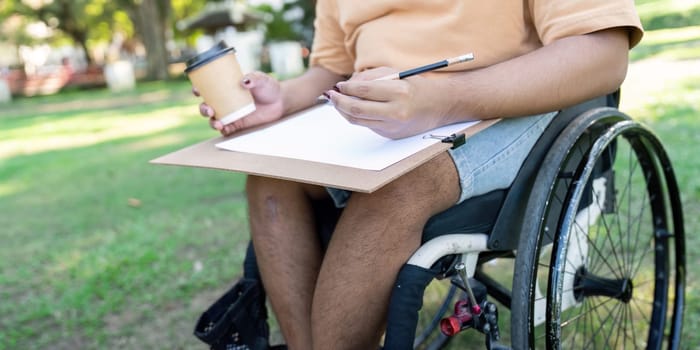 A close-up of a disabled artist in a wheelchair enjoys a coffee while preparing to sketch outdoors, showcasing creativity in a vibrant park.