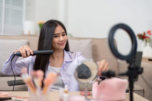 A beauty broker confidently styling her hair with a straightener while engaging her audience in a live broadcast, surrounded by makeup products and tools.