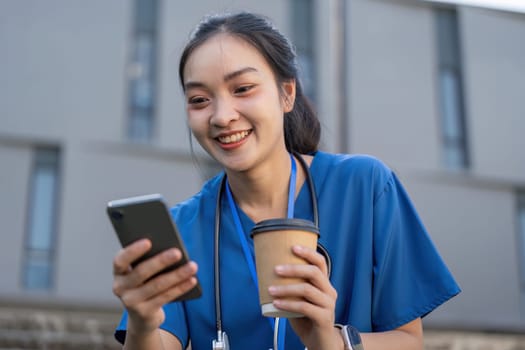 Cheerful nurse with a coffee cup engaged with her smartphone, taking a moment to relax in a healthcare setting.