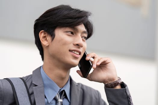 A confident young Asian businessman engaged in a phone conversation, showcasing professionalism and style in a work setting.