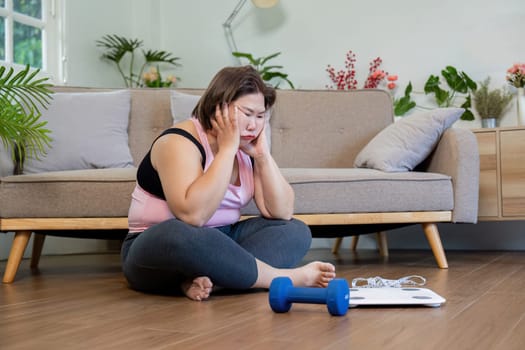 A plus size woman appears troubled by her weight loss progress while sitting on the floor, a scale and dumbbell nearby in a calming living area.