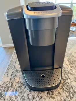 Castle Rock, Colorado, USA-April 18, 2023-Keurig coffee maker placed on a polished granite countertop in a modern kitchen. The coffee machine is shown alongside a matching Keurig coffee cup with a lid. The sleek black and stainless steel design complements the countertop elegant pattern, showcasing a contemporary kitchen appliance setup.
