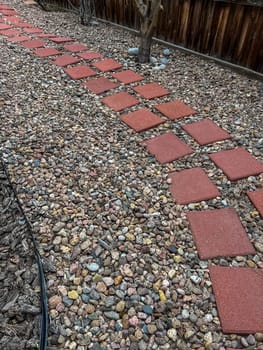 A close-up view of an aging retaining wall made of stacked concrete blocks, surrounded by a bed of decorative stones in various colors and sizes. The landscape shows signs of wear and is ready for renovation to restore its appeal and functionality.