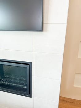 Castle Rock, Colorado, USA-May 14, 2023-A sleek, modern living room showcasing a tall tiled wall with a built-in electric fireplace and mounted flat-screen TV. The clean, geometric design includes recessed display shelves on the side and an integrated vent above. The minimalist aesthetic creates a sophisticated and functional living space.