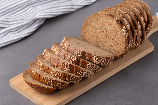 Freshly sliced sesame seed bread on a wooden cutting board with a striped kitchen towel in the background in a modern kitchen.